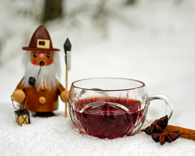 Festive wooden elf on snow with a mug of red wine